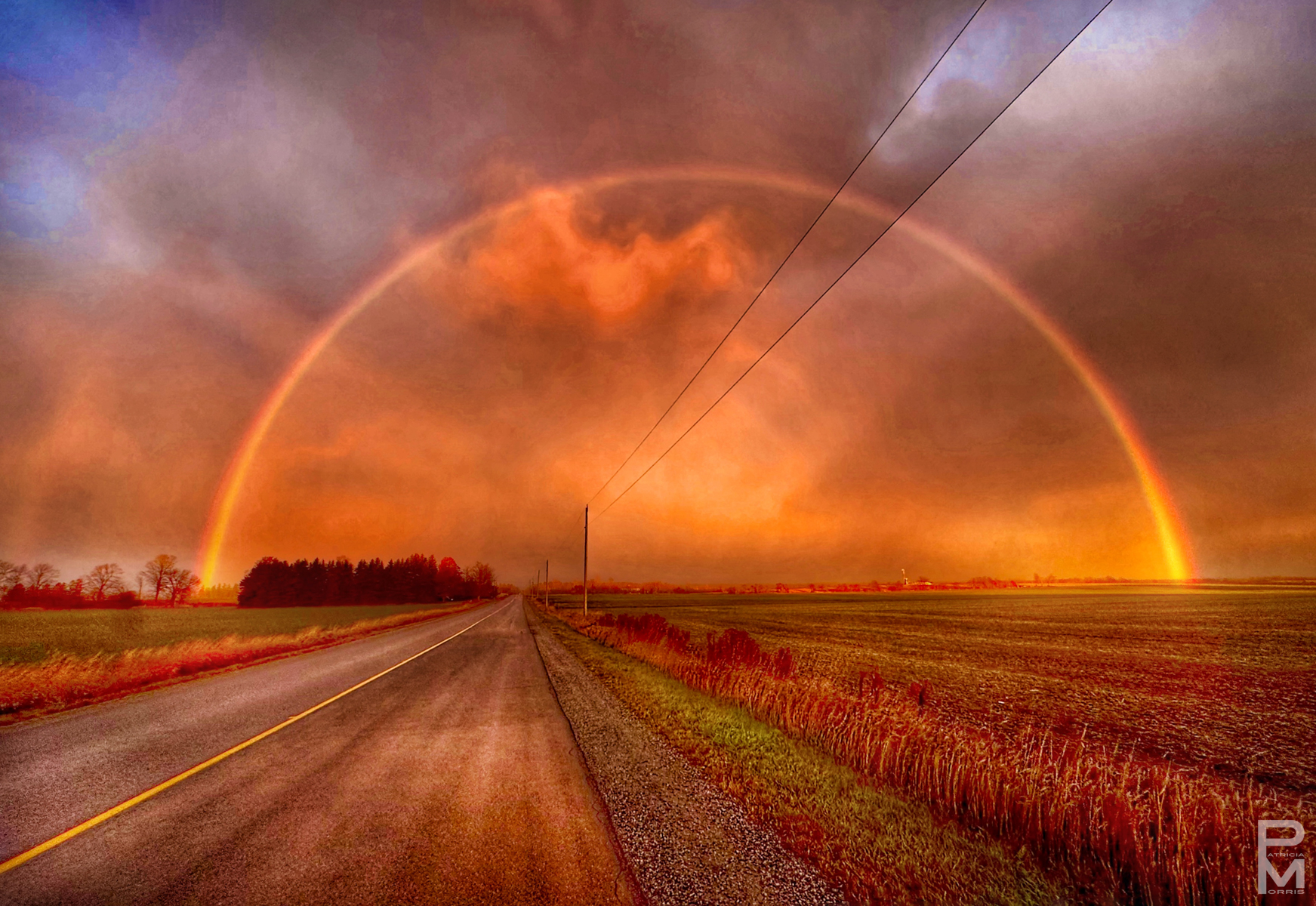 Digital photograph, landscape, view of a receding rural road at sunset with a full rainbow